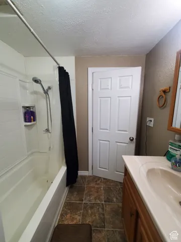 Bathroom with a textured ceiling, vanity, shower / bath combination with curtain, and a textured wall