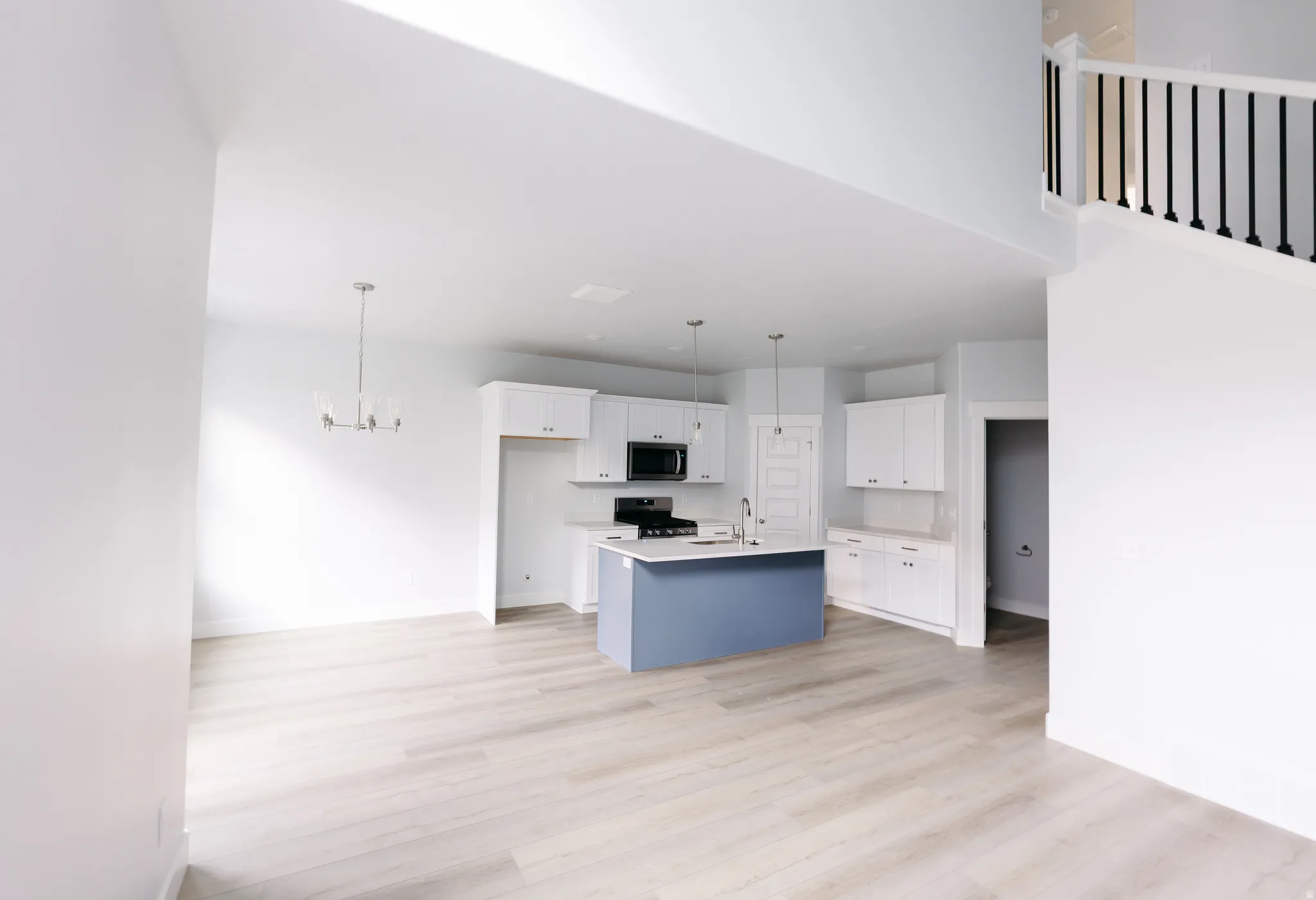 Kitchen with white cabinetry, a kitchen island with sink, light countertops, open floor plan, and pendant lighting