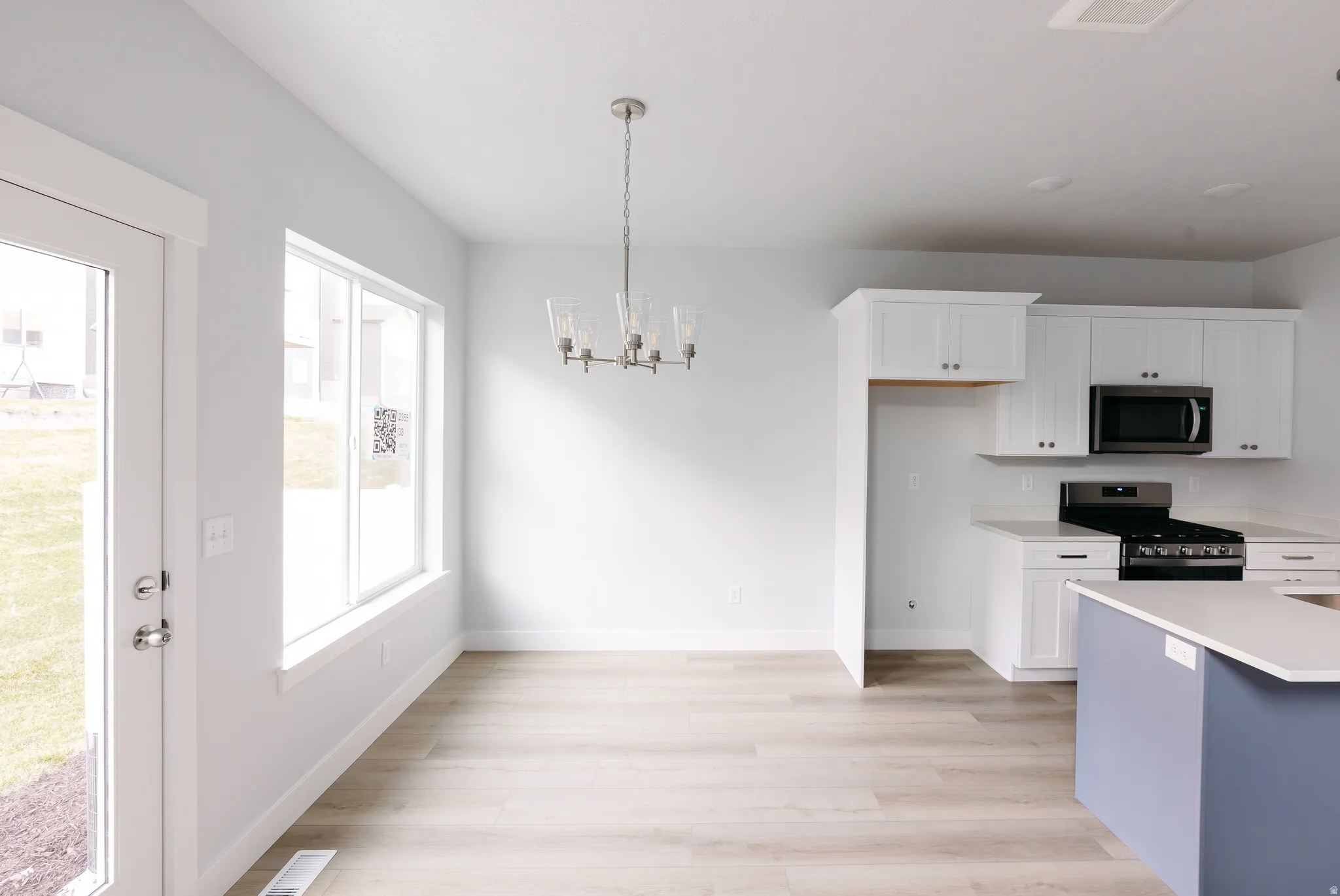 Kitchen with white cabinets, decorative light fixtures, appliances with stainless steel finishes, a chandelier, and light wood-style flooring
