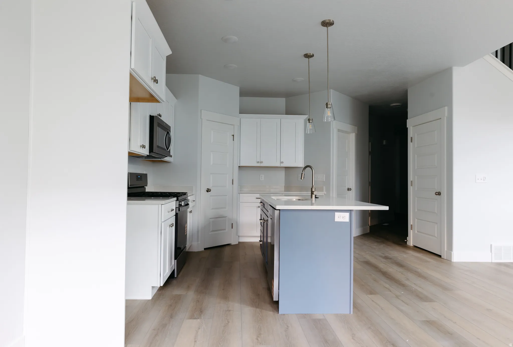 Kitchen with white cabinets, gas stove, a kitchen island with sink, decorative light fixtures, and black microwave