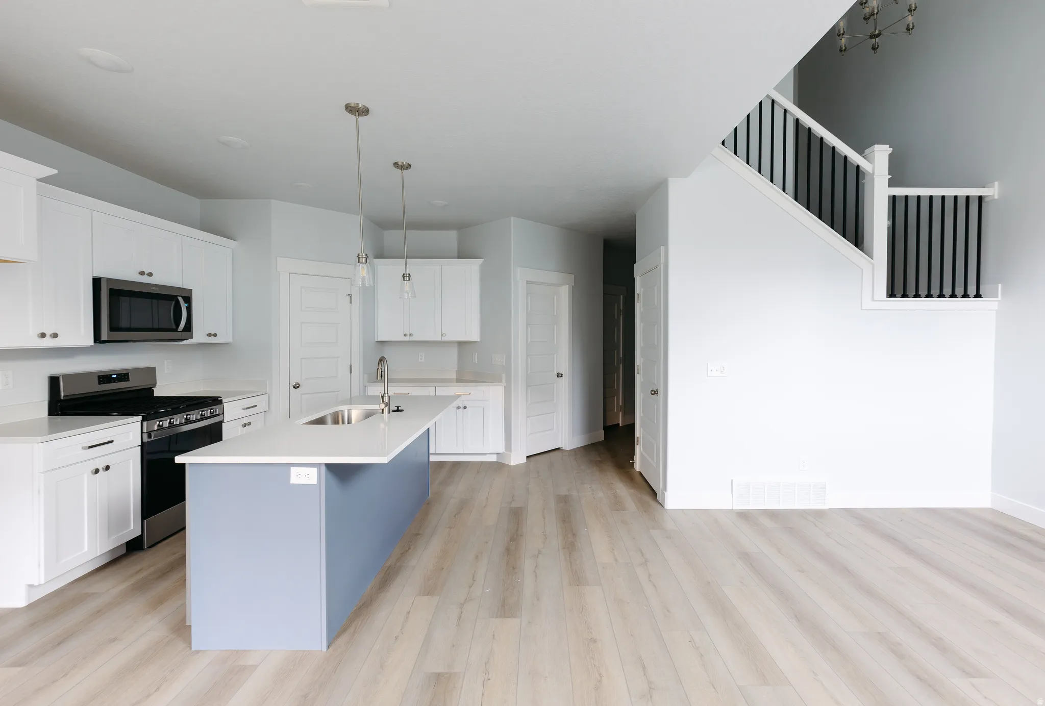 Kitchen with stainless steel appliances, white cabinets, a center island with sink, light wood finished floors, and hanging light fixtures