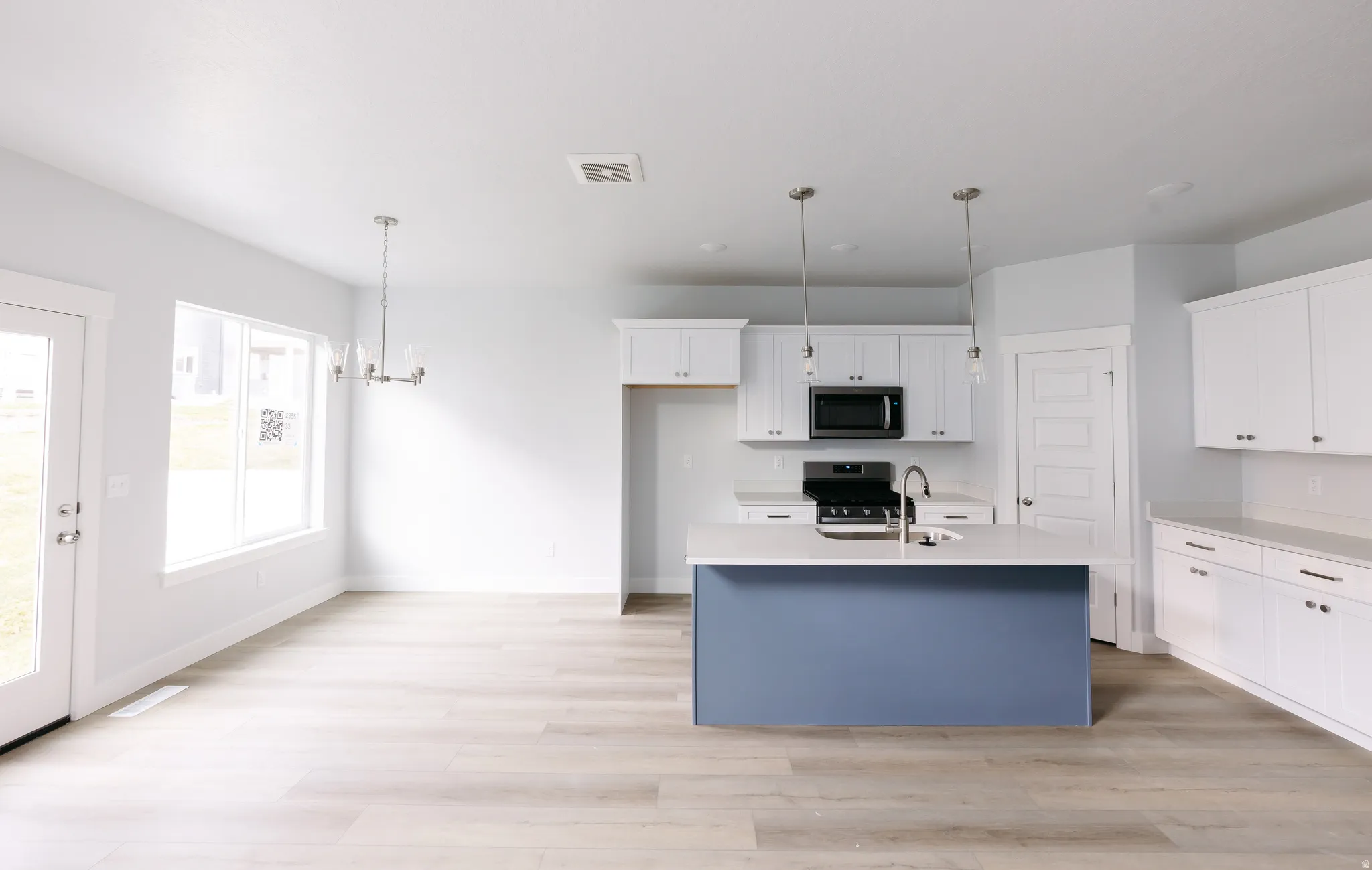 Kitchen with white cabinetry, an island with sink, decorative light fixtures, range with electric cooktop, and a chandelier