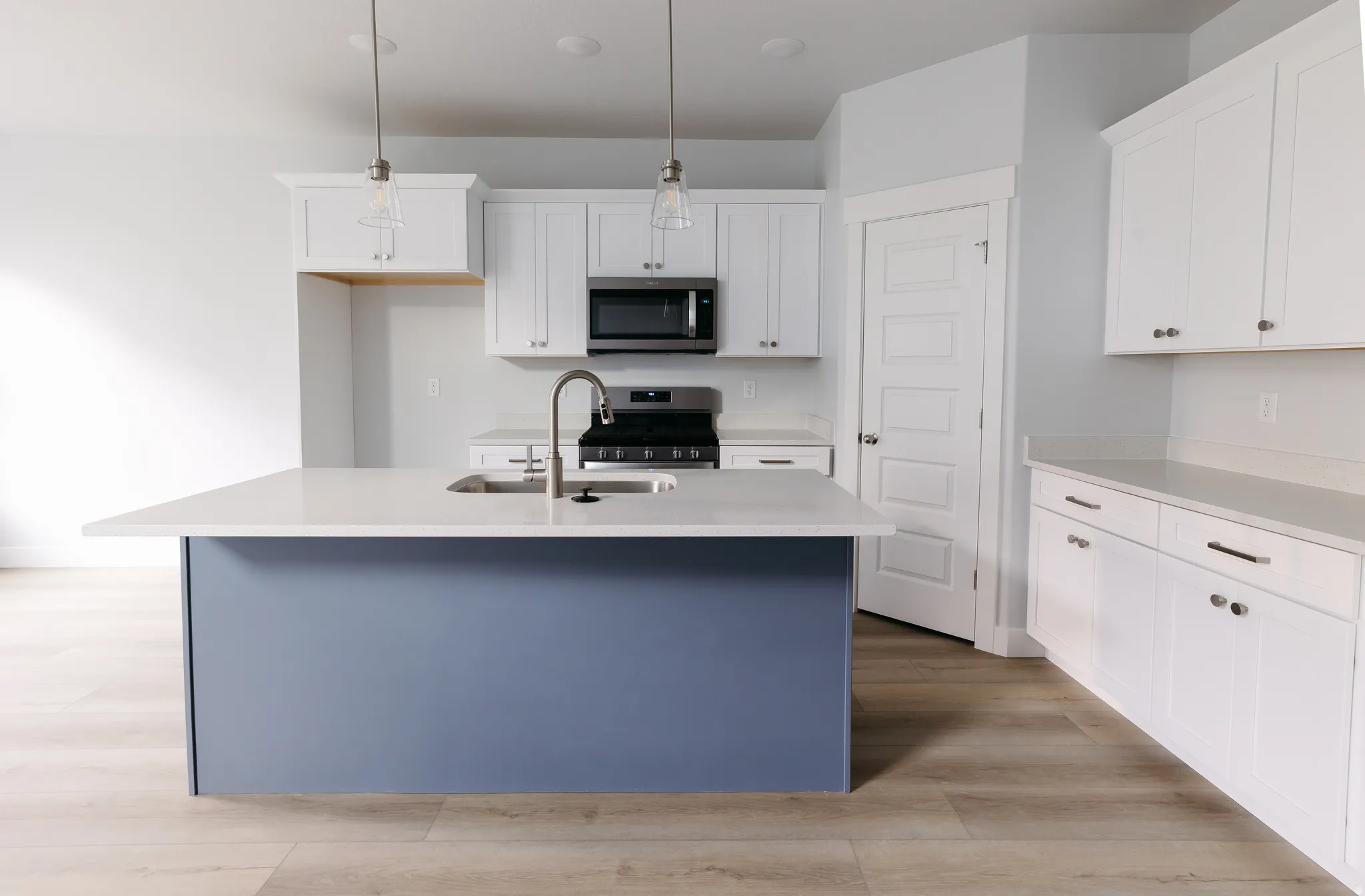 Kitchen featuring a center island with sink, decorative light fixtures, white cabinets, light wood-style flooring, and stainless steel appliances