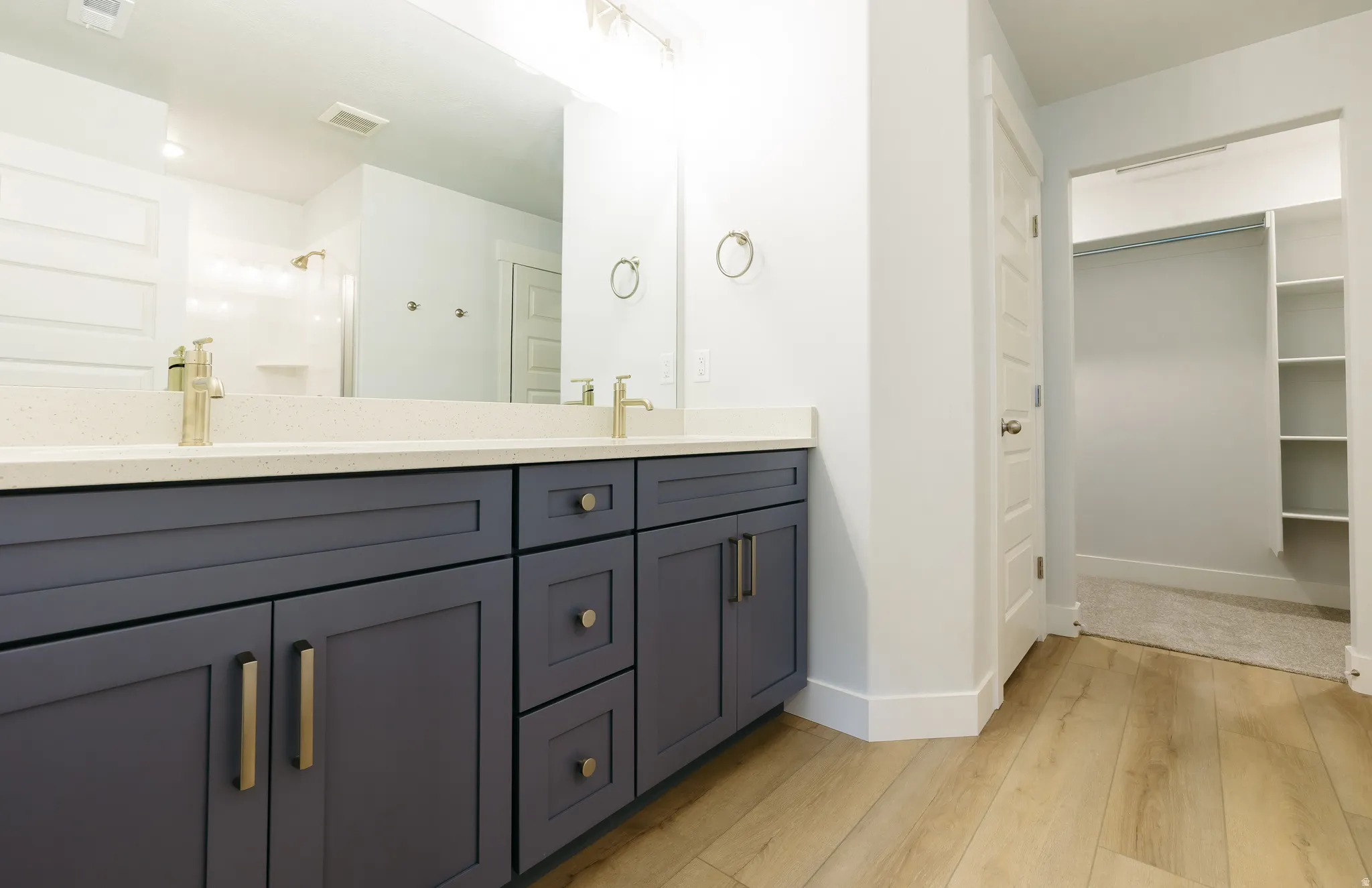 Full bathroom featuring double vanity, a spacious closet, a stall shower, and light wood-style flooring