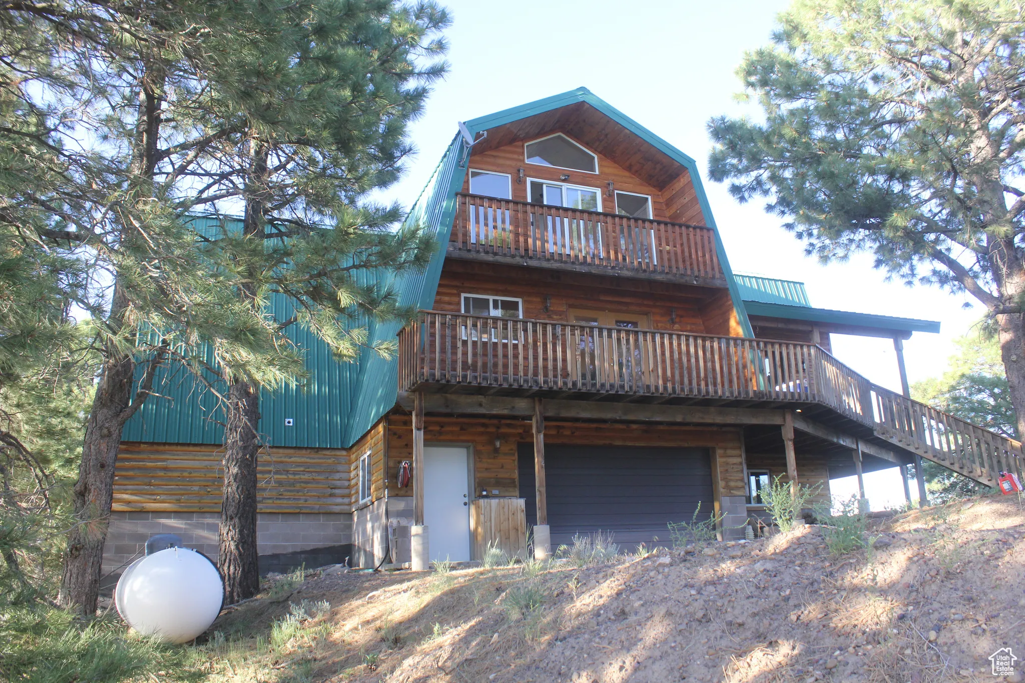 Back of house with a gambrel roof, an attached garage, a balcony, a deck, and log veneer siding