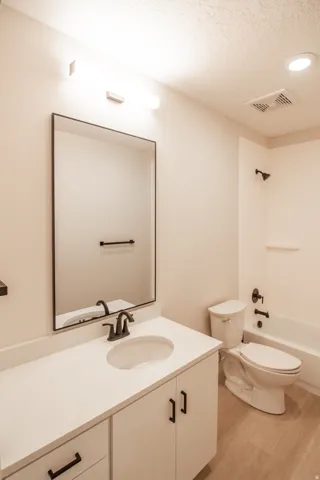 Full bath with vanity, a textured ceiling, light wood-style flooring, and bathtub / shower combination