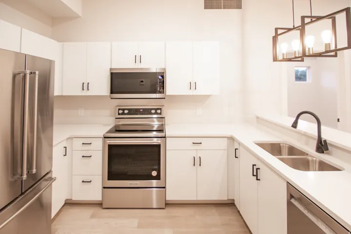 Kitchen featuring appliances with stainless steel finishes, decorative light fixtures, white cabinetry, light wood-type flooring, and light stone counters