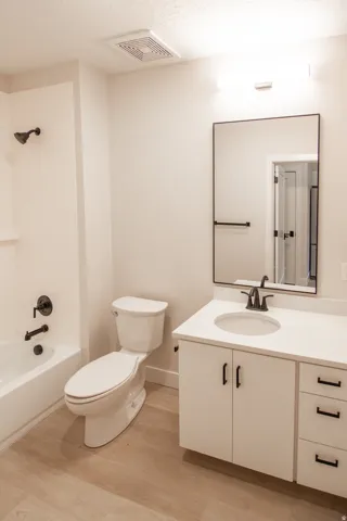 Bathroom with vanity, shower / bath combination, light wood-style floors, and a textured ceiling