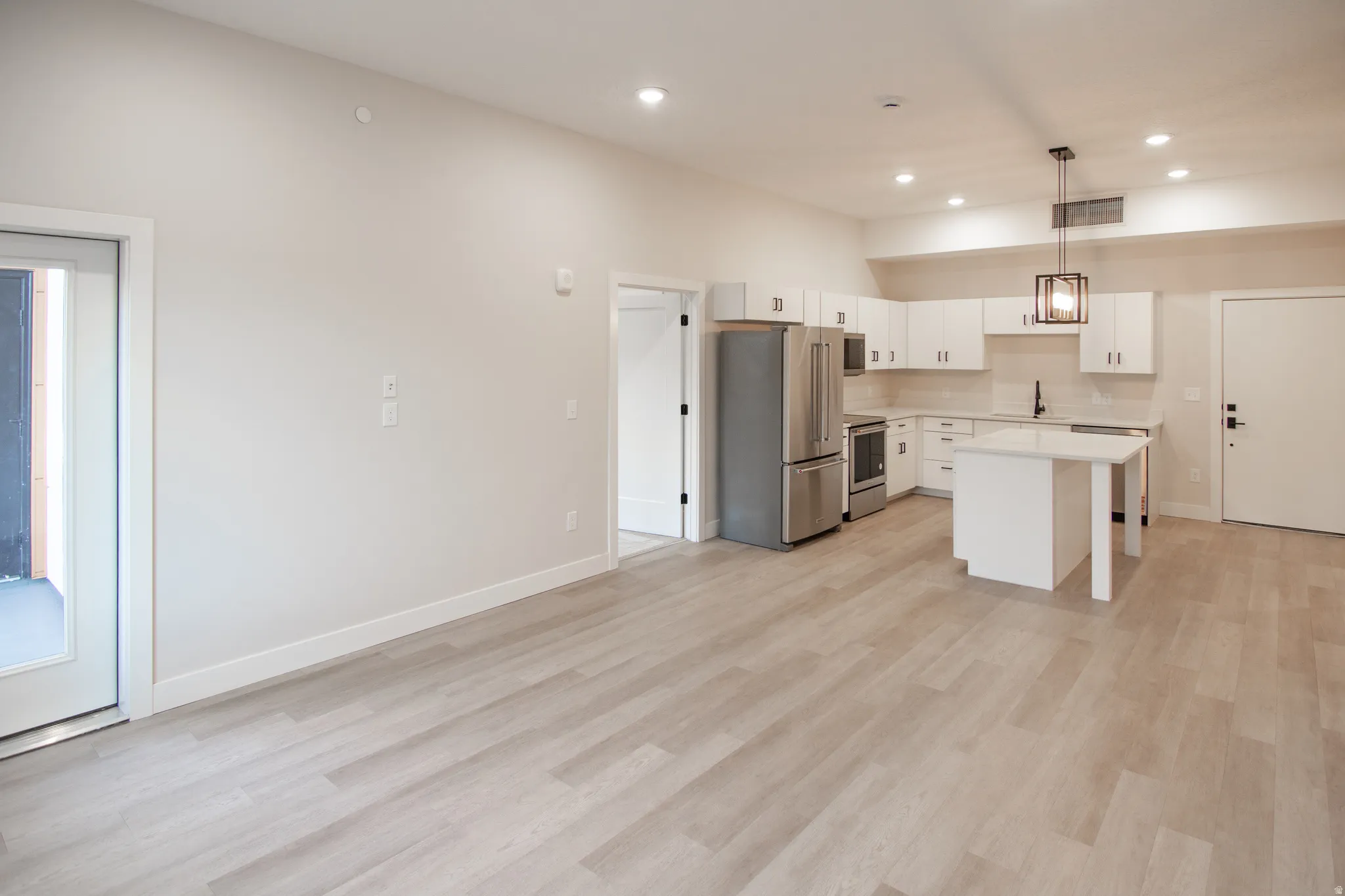 Kitchen with appliances with stainless steel finishes, light countertops, white cabinetry, decorative light fixtures, and a kitchen island