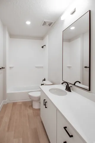 Bathroom with vanity, light wood finished floors, a textured ceiling, shower / washtub combination, and recessed lighting