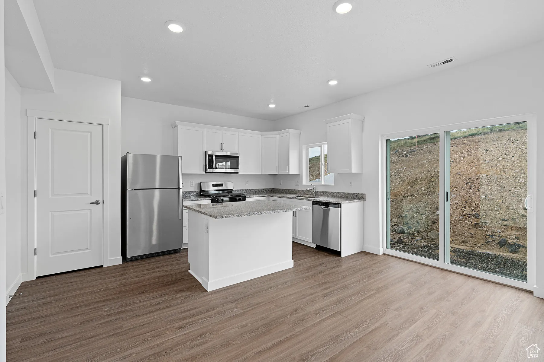 Kitchen featuring appliances with stainless steel finishes, white cabinets, dark wood-type flooring, recessed lighting, and a kitchen island