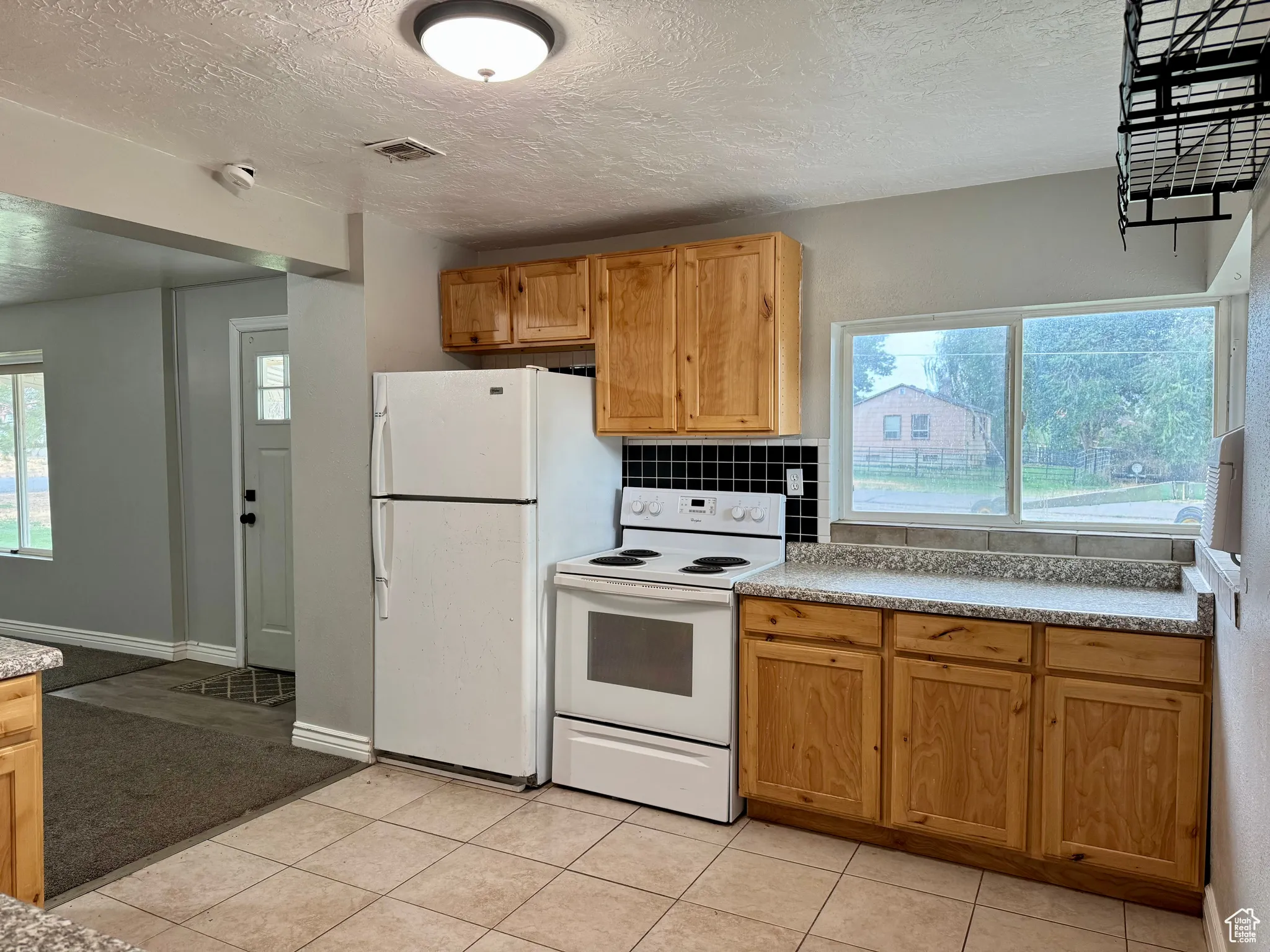 Kitchen with white appliances, a textured ceiling, light countertops, light tile patterned floors, and tasteful backsplash