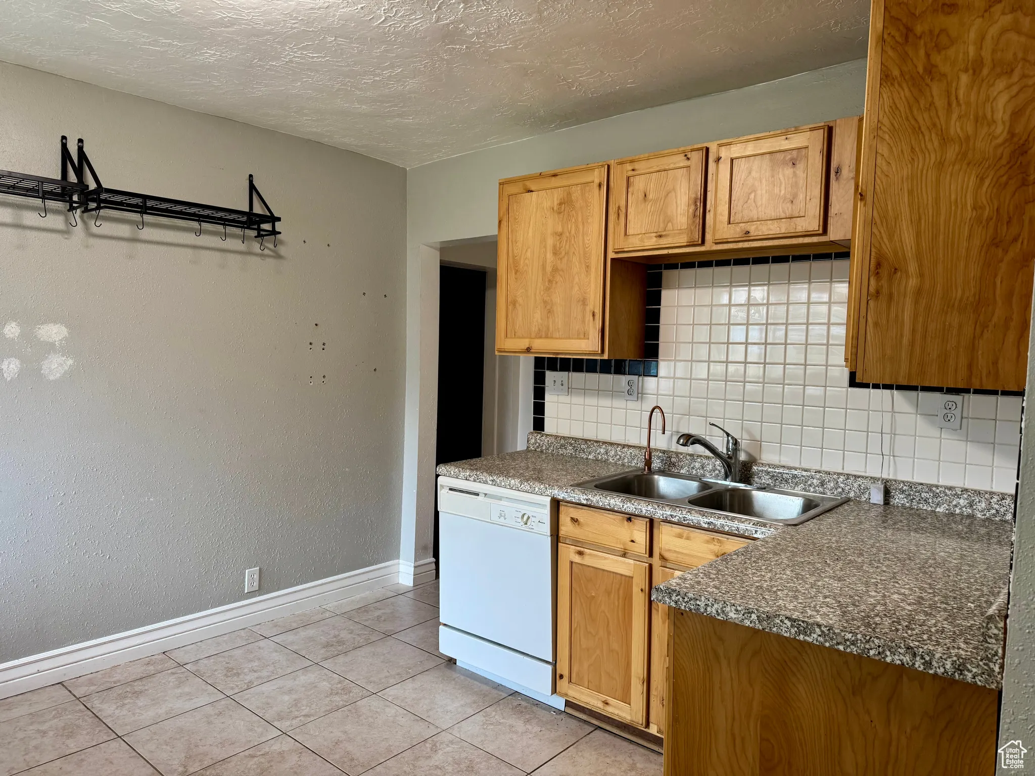 Kitchen with backsplash, a textured ceiling, dishwasher, light tile patterned flooring, and dark countertops
