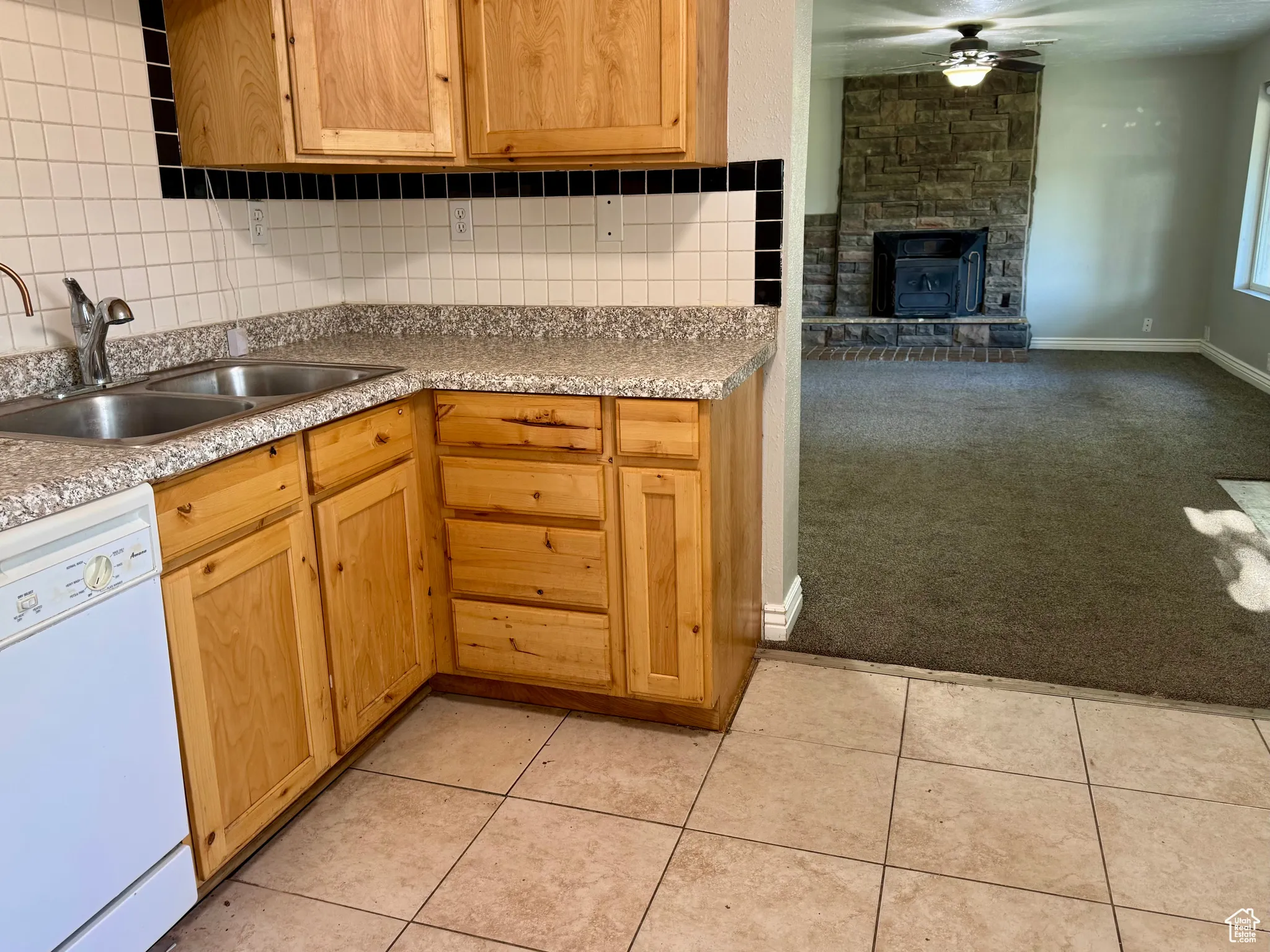 Kitchen with white dishwasher, decorative backsplash, a fireplace, ceiling fan, and light countertops