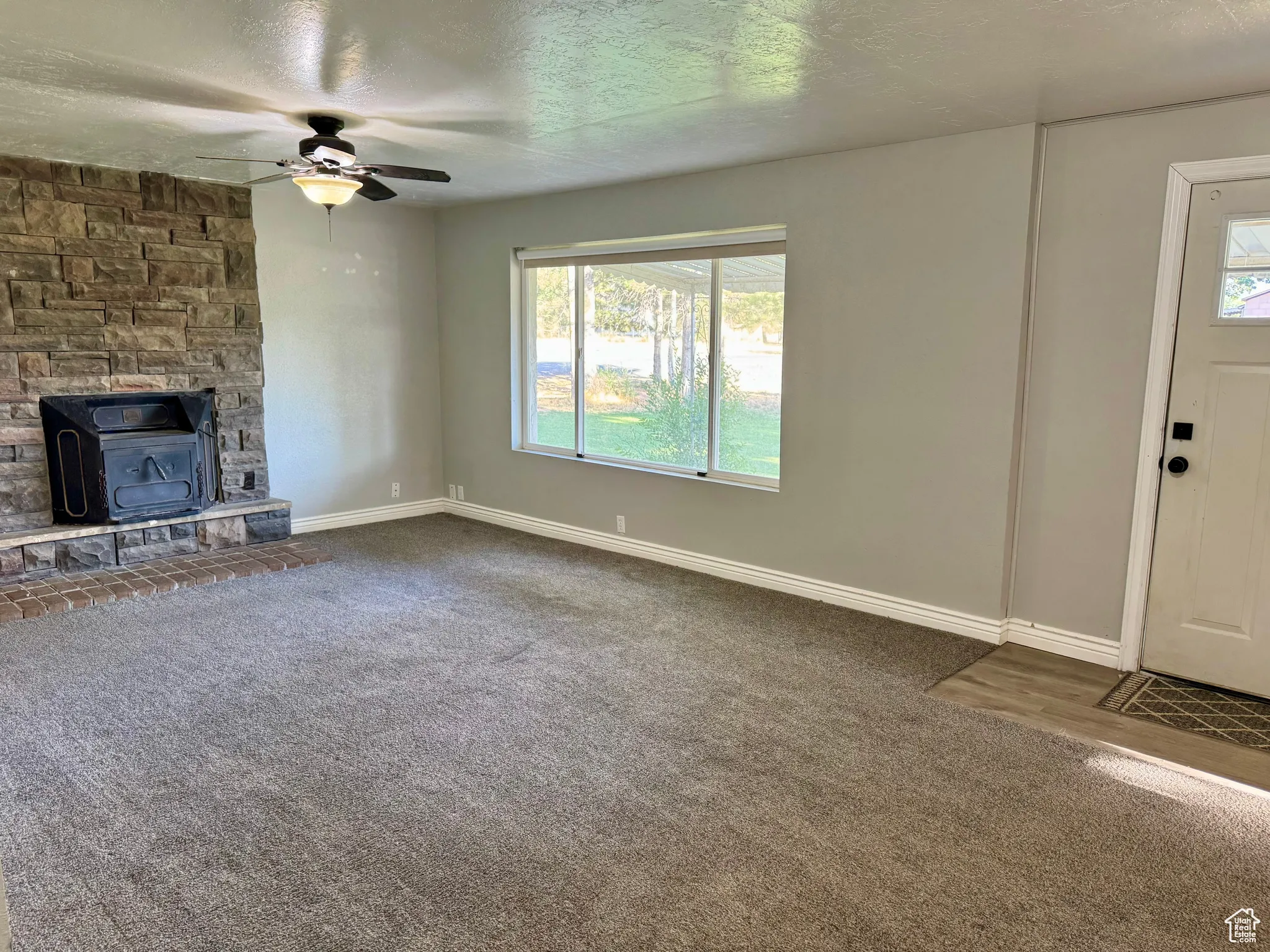 Unfurnished living room featuring carpet, a textured ceiling, a ceiling fan, and a wood stove
