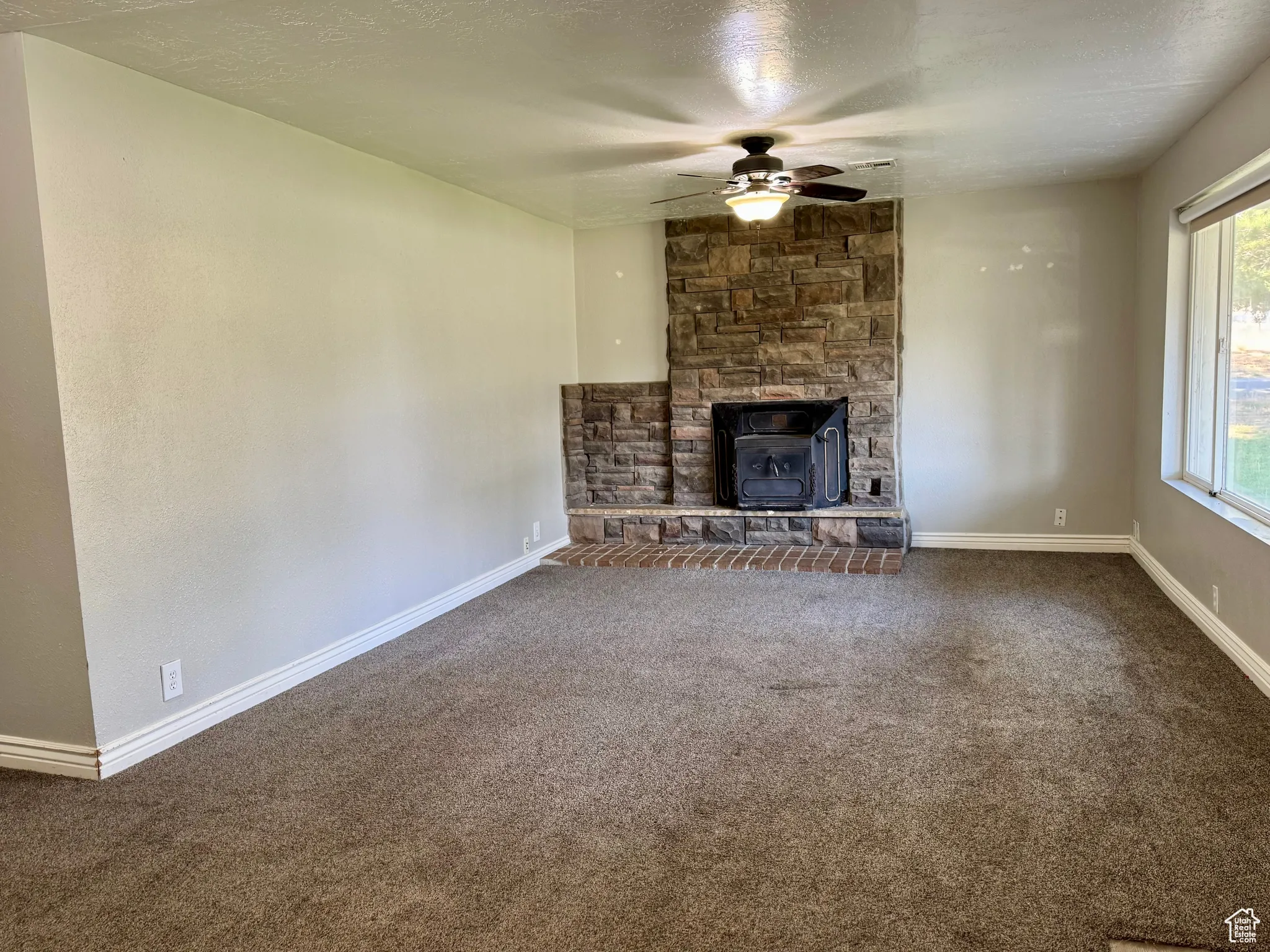 Unfurnished living room featuring carpet floors, a textured ceiling, a ceiling fan, and a fireplace