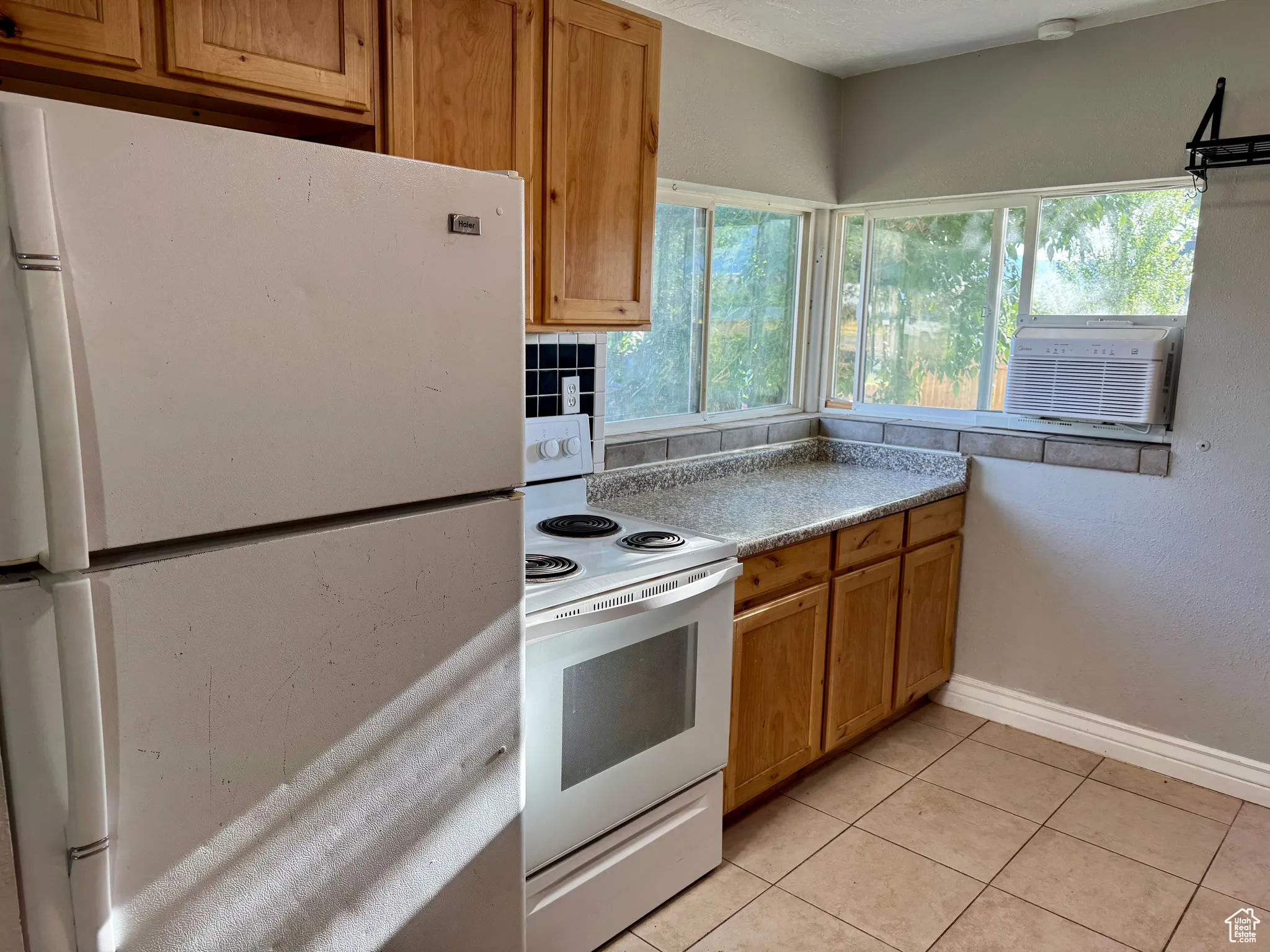 Kitchen with white appliances, light countertops, brown cabinetry, light tile patterned flooring, and cooling unit