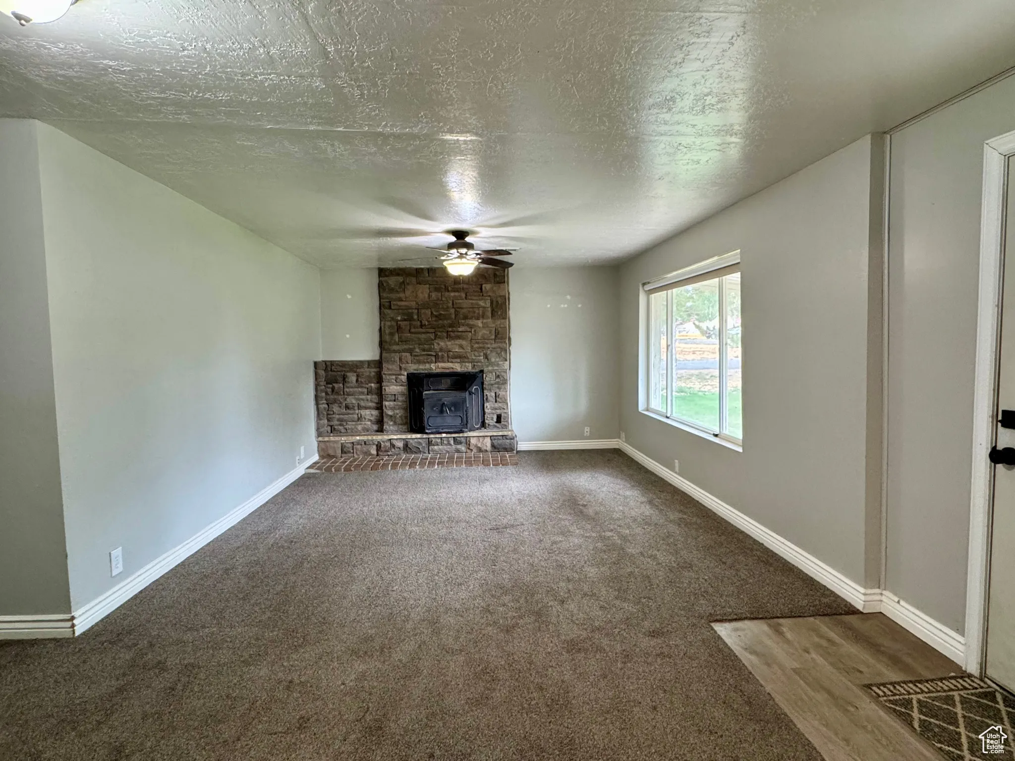 Unfurnished living room featuring a fireplace, dark colored carpet, a ceiling fan, and a textured ceiling