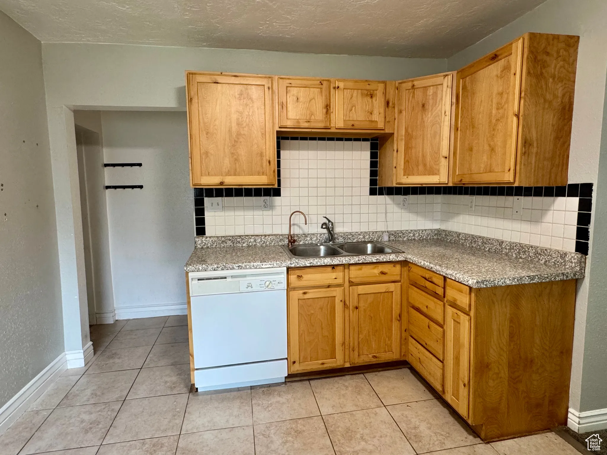 Kitchen with tasteful backsplash, dishwasher, a textured ceiling, light countertops, and light tile patterned flooring