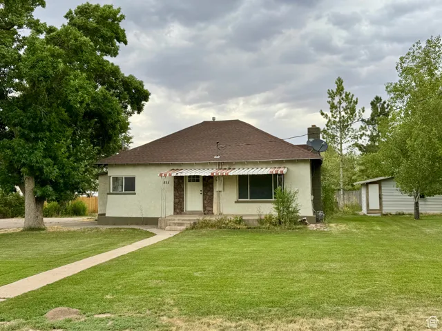 View of front of home featuring roof with shingles, stucco siding, a front lawn, and a chimney