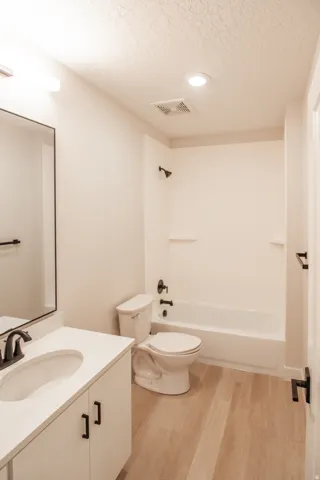Full bathroom with a textured ceiling, vanity, light wood finished floors, and bathtub / shower combination