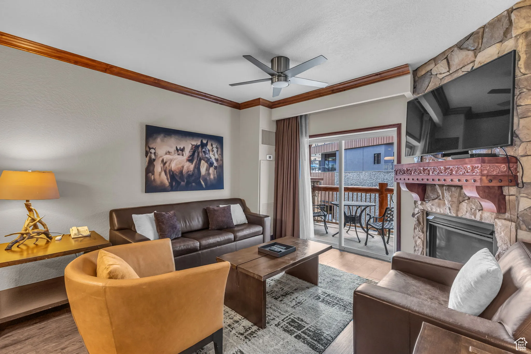 Living area with wood finished floors, crown molding, ceiling fan, and a stone fireplace