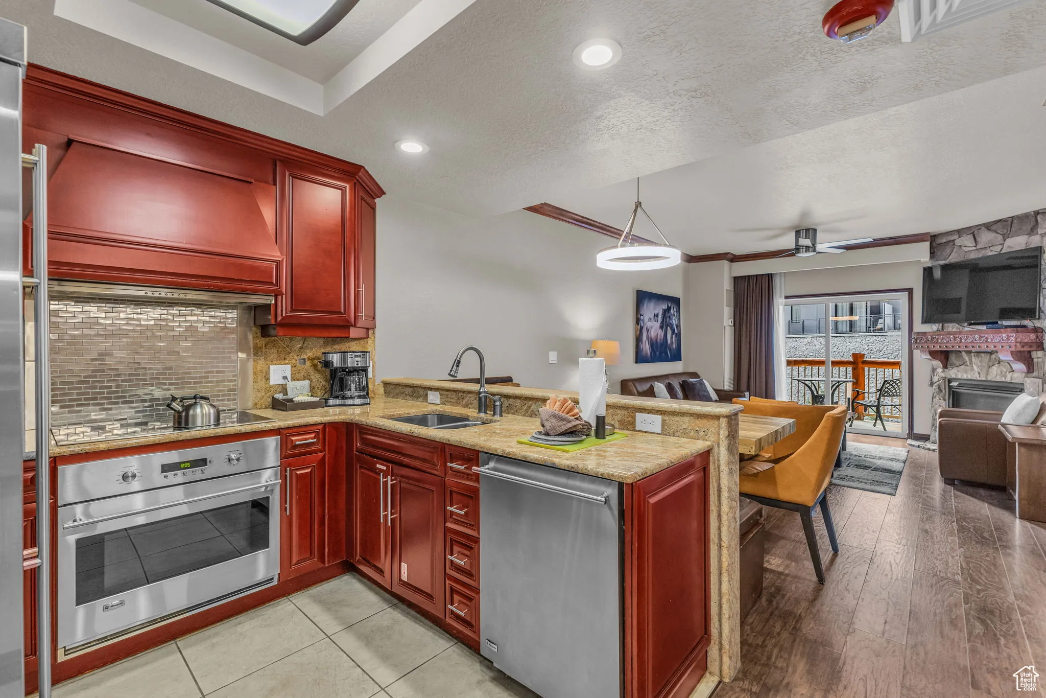 Kitchen with reddish brown cabinets, light stone countertops, a peninsula, stainless steel appliances, and a textured ceiling
