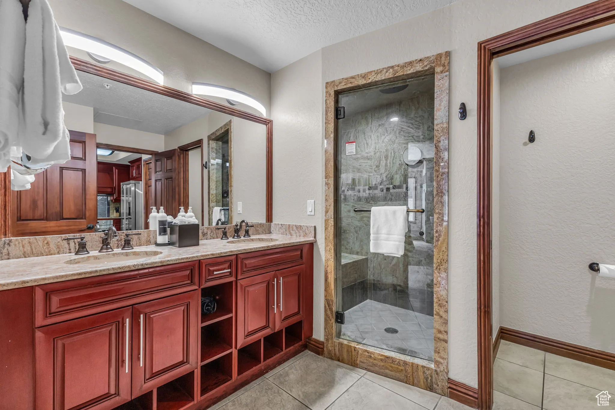 Full bath featuring a textured ceiling, light tile patterned floors, a shower stall, double vanity, and a textured wall
