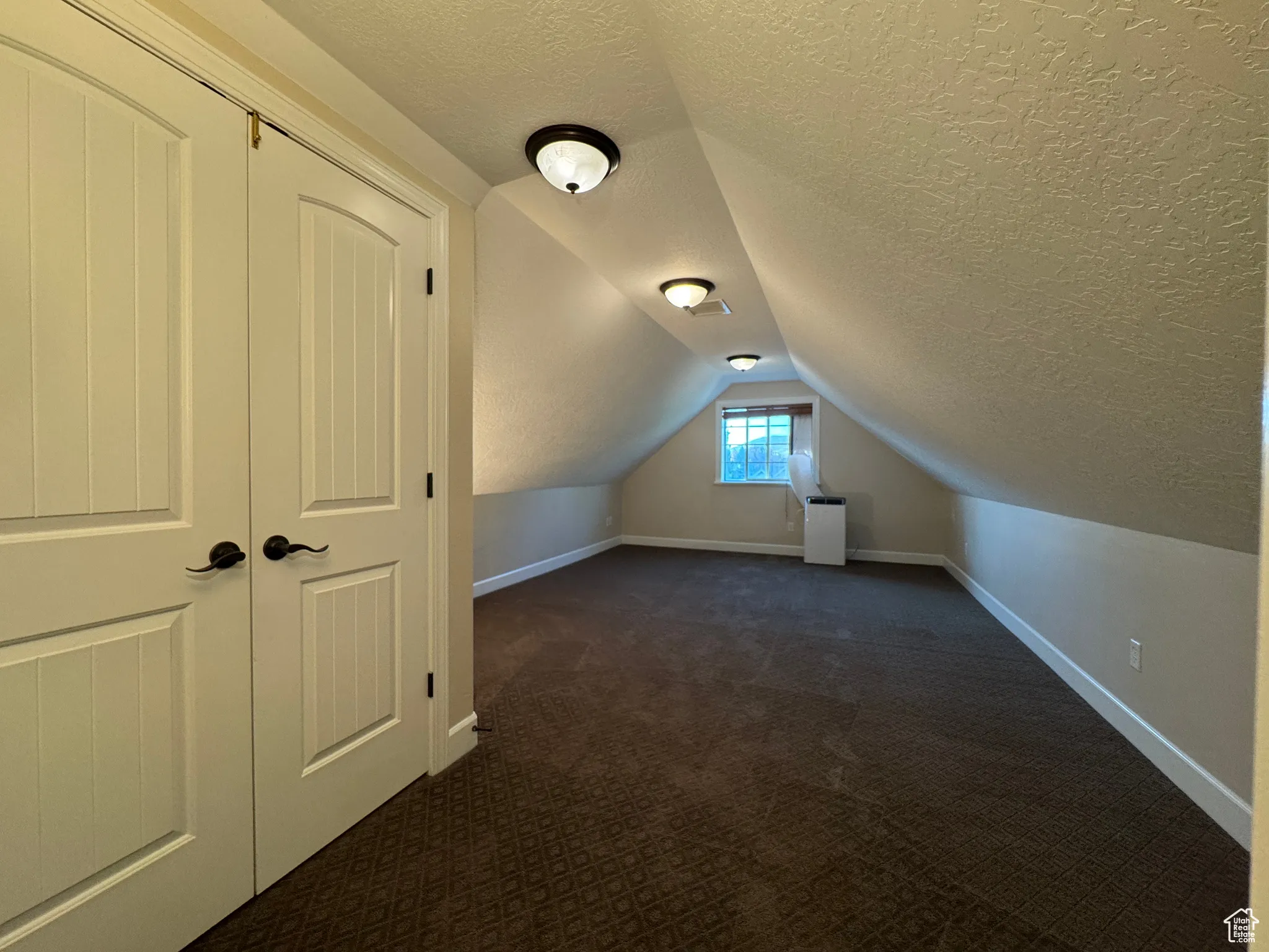 Additional living space with a textured ceiling, dark carpet, and lofted ceiling