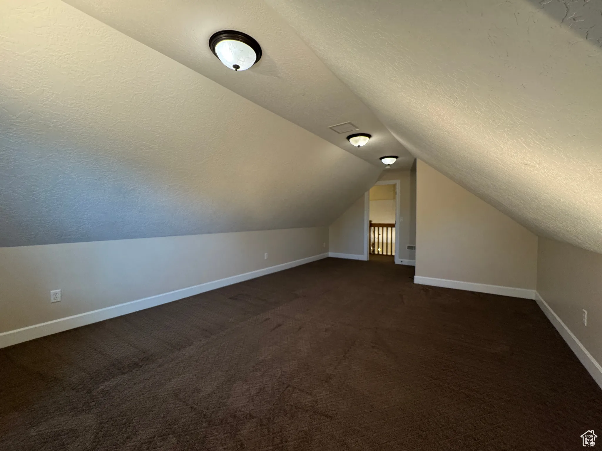 Bonus room featuring a textured ceiling, dark carpet, and vaulted ceiling