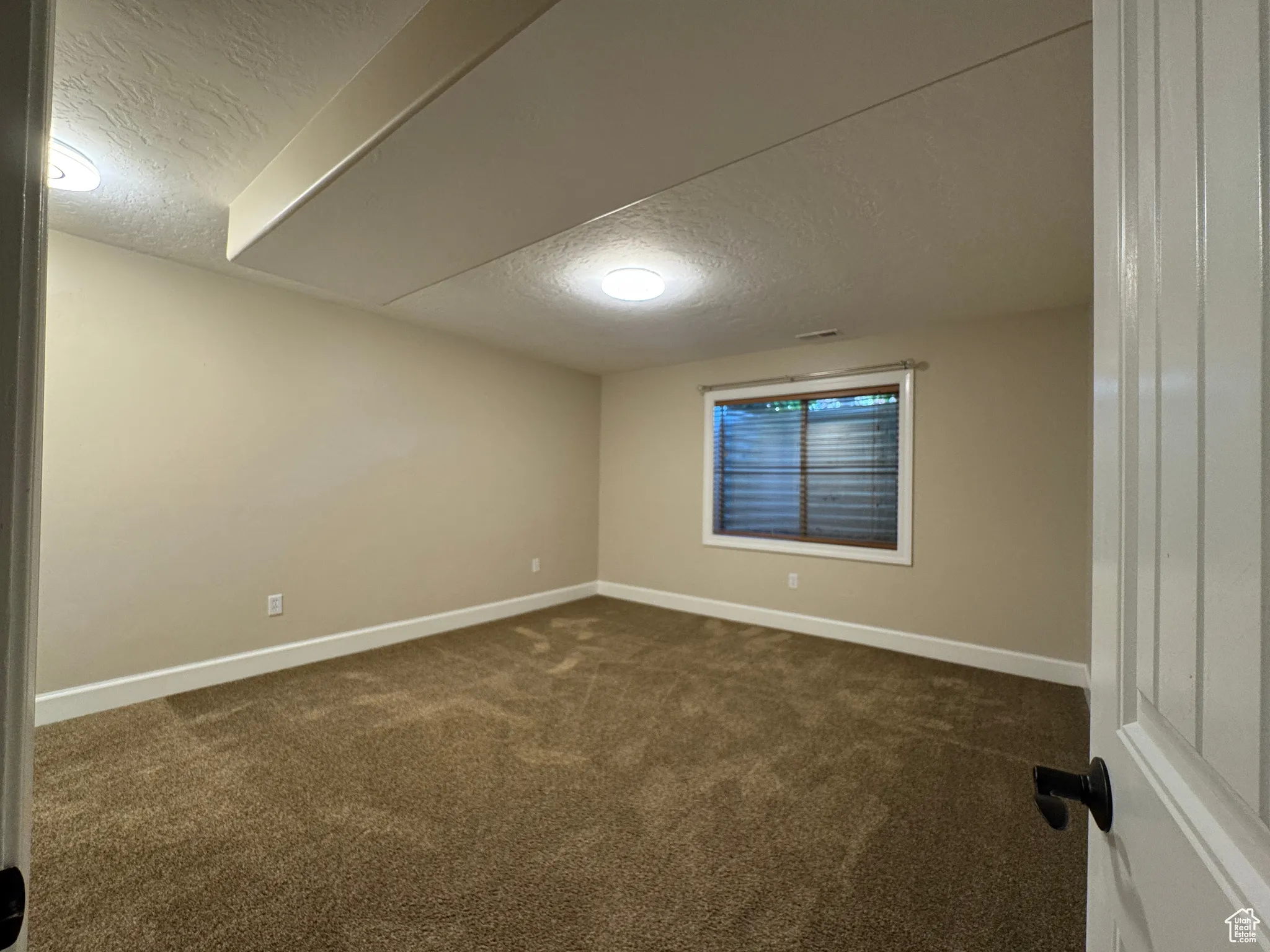 Unfurnished room with a textured ceiling and dark colored carpet