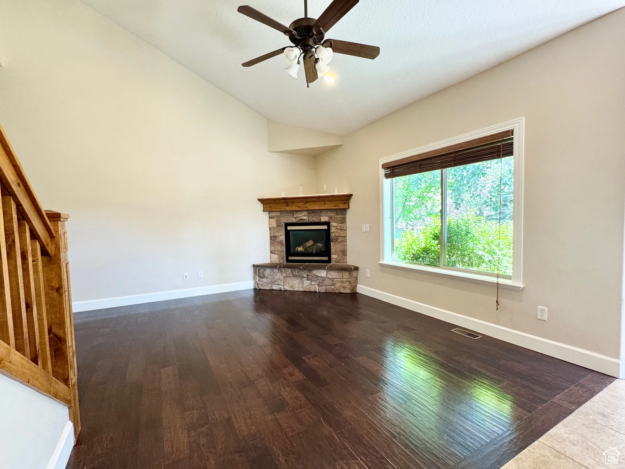 Unfurnished living room with dark wood-type flooring, a stone fireplace, a ceiling fan, stairway, and high vaulted ceiling