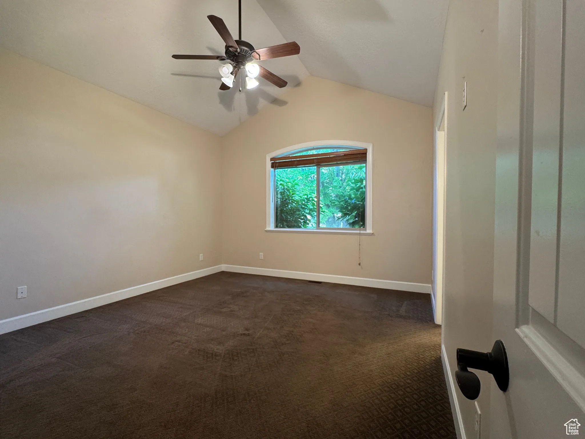 Empty room with vaulted ceiling, dark colored carpet, and a ceiling fan