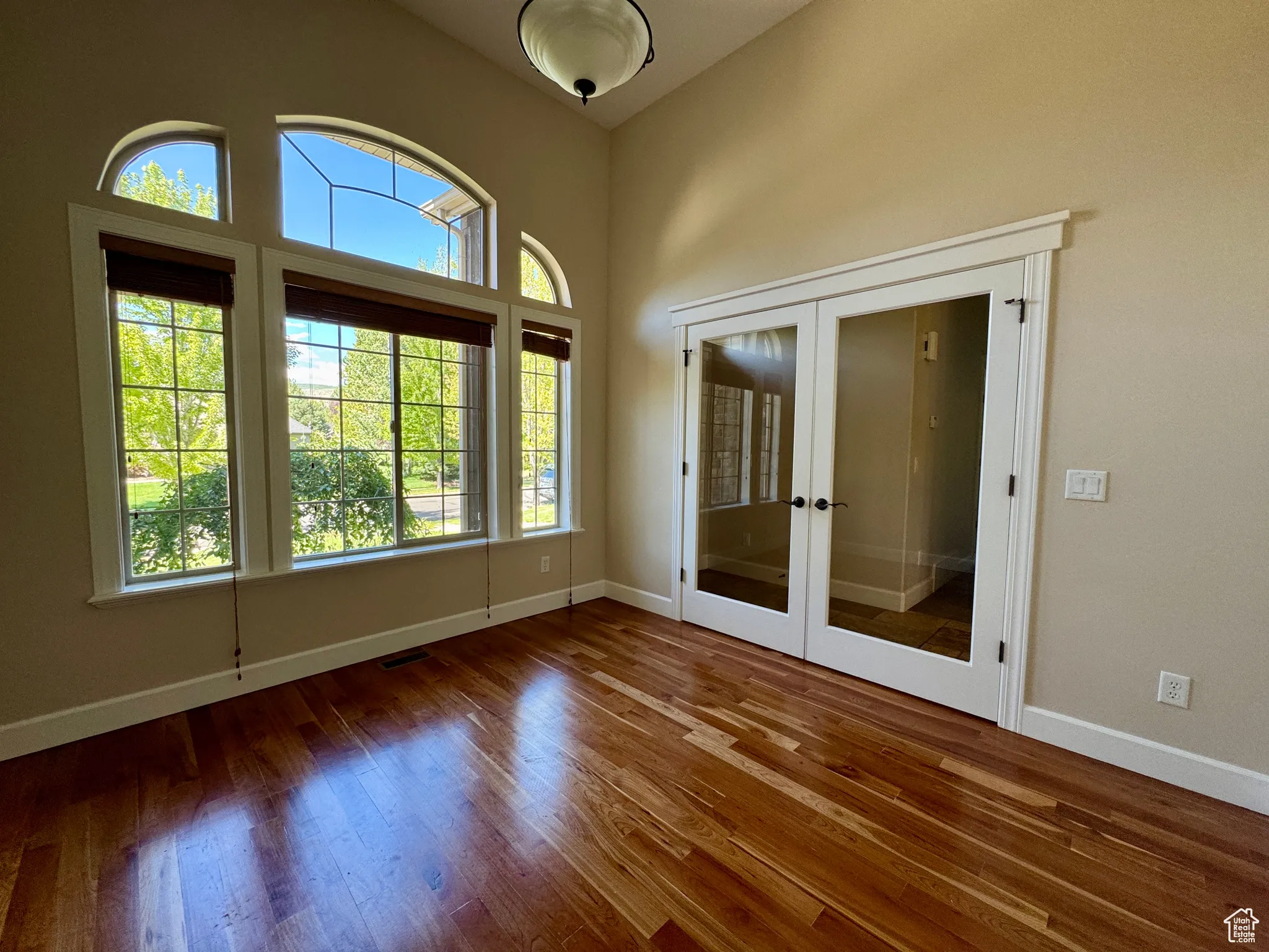 Empty room featuring french doors, wood finished floors, and a towering ceiling