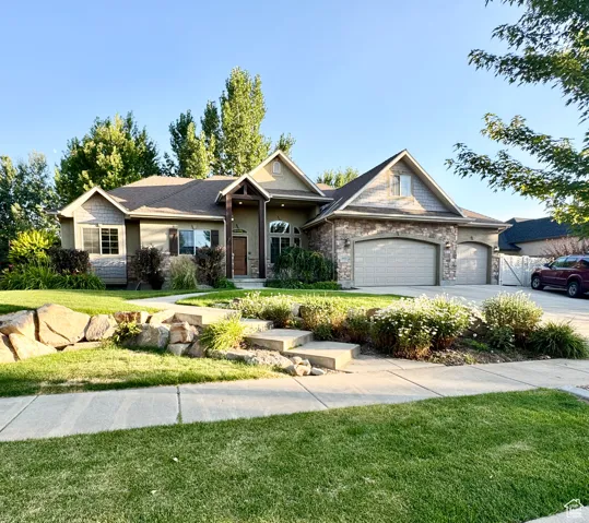 View of front of property with a front lawn, an attached garage, stone siding, and driveway