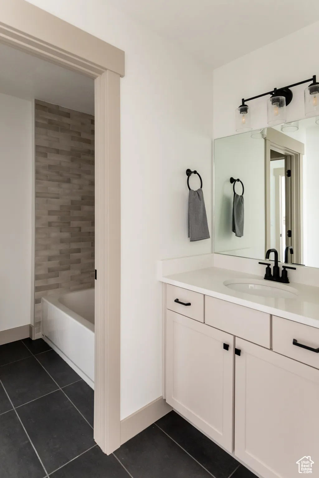 Bathroom with vanity, dark tile patterned flooring, and shower / bathtub combination