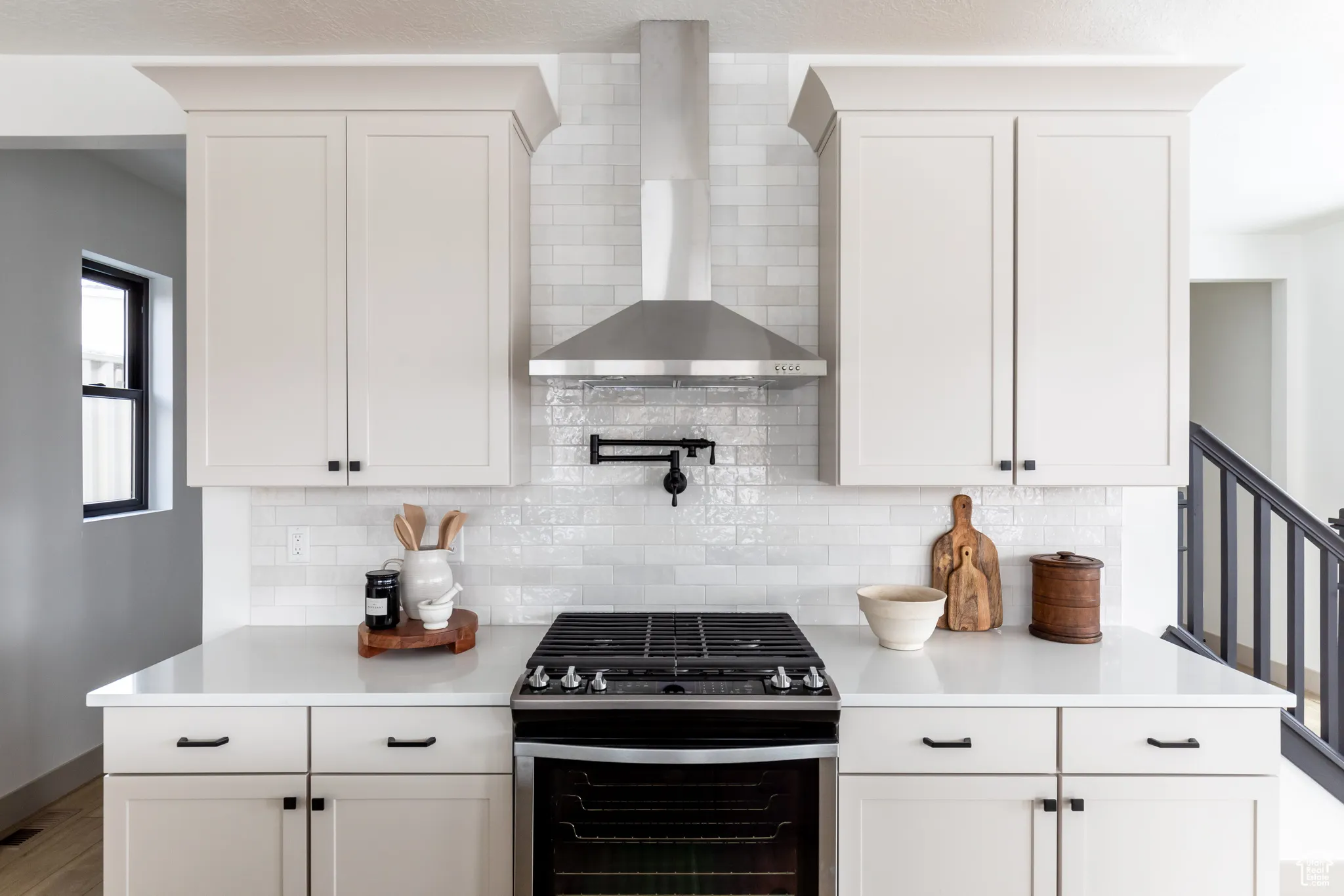 Kitchen featuring gas stove, wall chimney exhaust hood, decorative backsplash, and white cabinetry