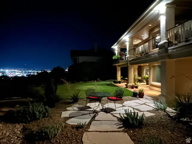 Yard at night featuring a balcony, a patio, and a lawn