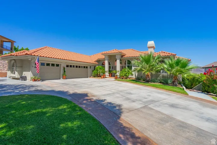 Mediterranean / spanish-style home with a tile roof, an attached garage, concrete driveway, stucco siding, and a front lawn