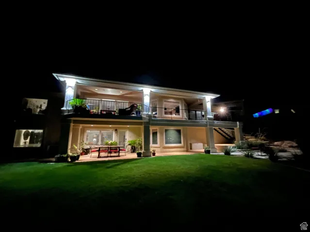 Back of house at twilight featuring a lawn, a patio, a balcony, and stairway
