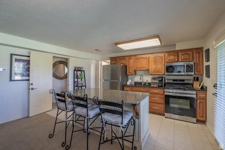 Kitchen with brown cabinetry, appliances with stainless steel finishes, a kitchen breakfast bar, a kitchen island, and dark stone counters