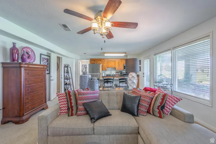 Living room featuring ceiling fan, light colored carpet, and a textured ceiling