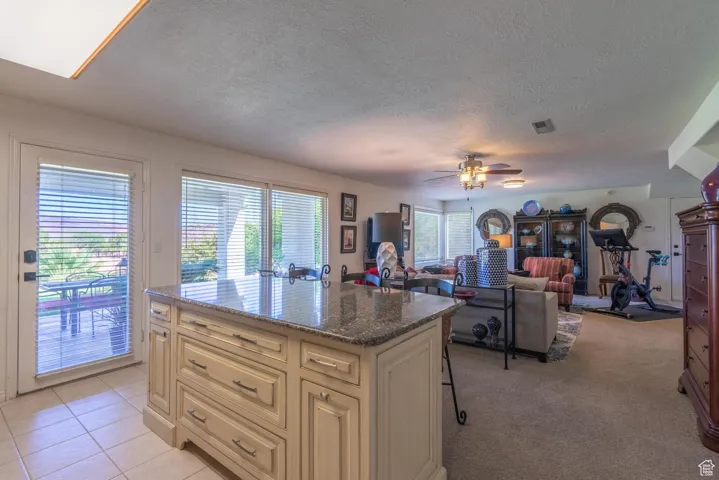 Kitchen featuring dark stone counters, a kitchen bar, a kitchen island, a textured ceiling, and a ceiling fan