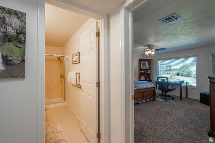 Hall featuring a textured ceiling, a desk, carpet flooring, and tile patterned flooring