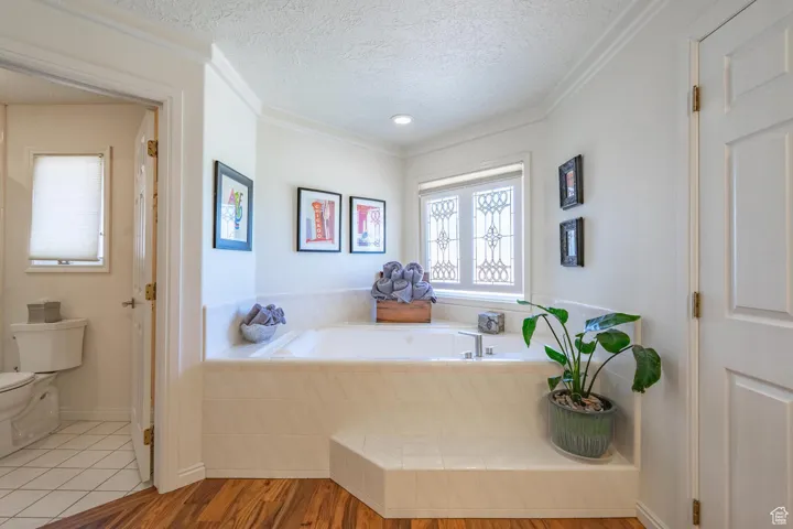 Full bath with wood finished floors, a textured ceiling, a garden tub, and crown molding