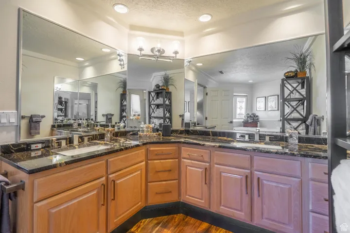 Full bathroom with a textured ceiling, dark wood-style floors, double vanity, crown molding, and recessed lighting