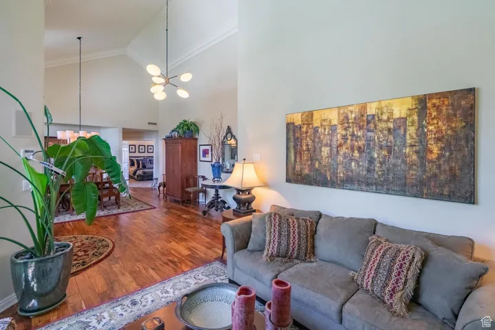 Living room with high vaulted ceiling, wood finished floors, a chandelier, and crown molding