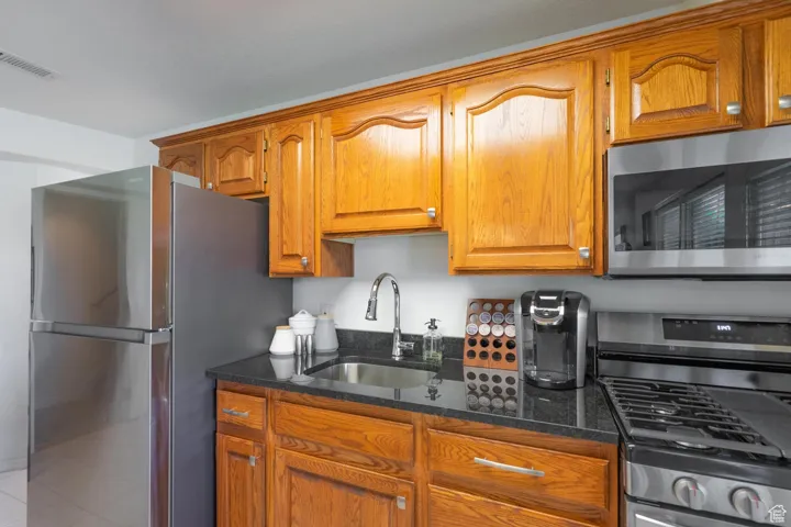 Kitchen featuring appliances with stainless steel finishes, dark stone counters, brown cabinets, and tile patterned floors