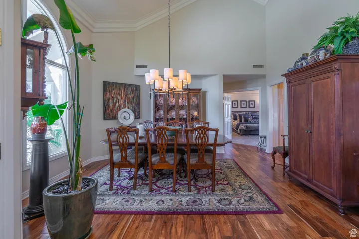 Dining room featuring dark wood-style flooring, ornamental molding, high vaulted ceiling, and a chandelier