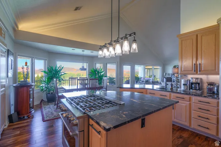 Kitchen featuring gas stove, dark wood-type flooring, dark stone counters, hanging light fixtures, and high vaulted ceiling
